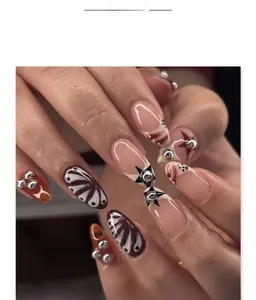 Detail of short almond press-on nails with brown smudge, black stars, and 3D silver beads