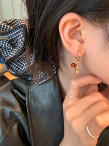 Détail de la boucle d'oreille pendante cacahuète perlée avec perle rouge et bagues d'or