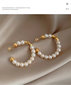 Detail of C-shaped gold plated pearl earrings on champagne silk fabric background