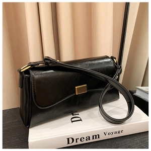 Nahaufnahme einer schwarzen Leder-Achseltasche mit goldener Schnalle auf einem Deko-Buch