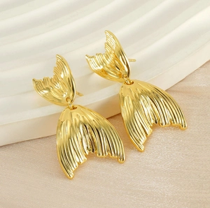 Détail de boucles d'oreilles queue de poisson dorées avec texture sur fond satiné chic