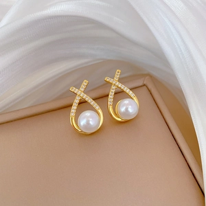 Elegant gold pearl stud earrings with crisscross zircon inlay on a luxury jewelry box