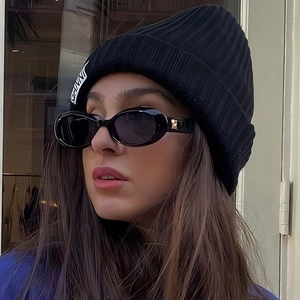 Close-up of black pleated beanie with woven label and oval sunglasses with gold hardware