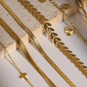 Set of gold cross pendant necklaces and leaf charm chains on textured stone background