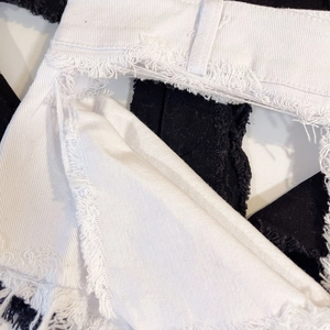 Détail d'un short en jean montrant des bords effilochés et un patchwork noir et blanc
