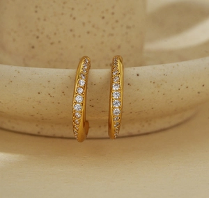 Macro detail of gold C-shaped earrings with micro-pave cubic zirconia on ceramic base