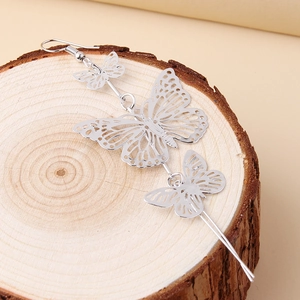 Macro shot of silver hollow butterfly drop earrings on a natural wood surface