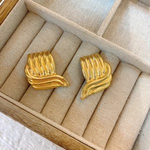 Boucles d'oreilles carrées dorées avec texture ondulée dans une boîte à bijoux en velours