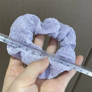 Ausmessen des hellvioletten Falten-Haargummis mit einem Lineal, Durchmesser ca. 11 cm