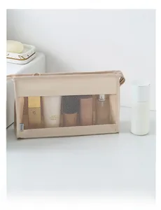 Detail view of the beige mesh toiletry bag with zipper and Travel label on white surface