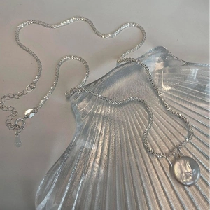 Macro shot of S925 sterling silver chain with baroque pearl pendant on shell plate