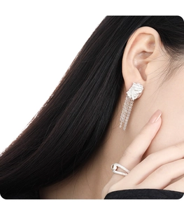 Detail of silver tassel earrings and textured pearl ring worn on a female model