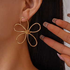 Close-up of a large gold hollow flower earring with elegant curved metal lines on a model