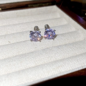 Detail view of round purple zircon earrings with silver prongs in a cream jewelry box