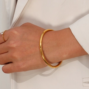 Polished 18K gold-plated stainless steel open bangle worn with a beige blazer suit