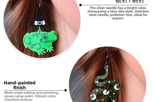 Detail of Halloween acrylic earrings featuring green frog with wizard hat and moon snake designs