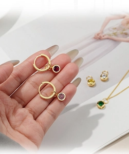 Detail of colorful round gemstone pendants on gold hoops displayed over magazine