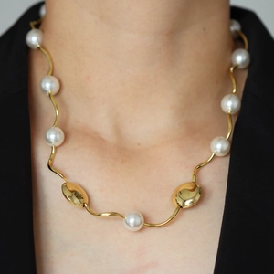 Detail of 18k gold plated wave chain necklace with white pearls on a model wearing black