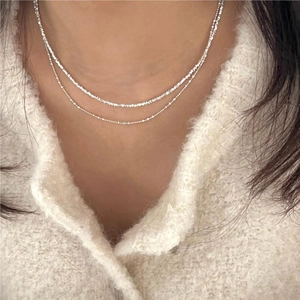 Detail of layered silver beaded necklace on model neck wearing a cream knit sweater