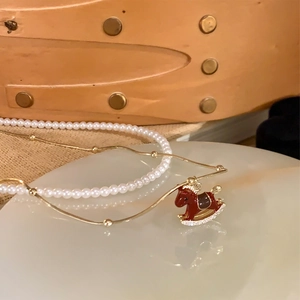 Macro view of gold-plated rocking horse pendant with red enamel and white pearls