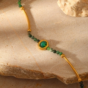 Macro detail of gold-plated curved tube necklace with faceted dark green natural stone beads