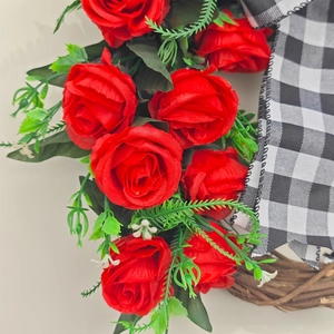 Close-up of red silk roses and black-white checkered bow on rustic branch wreath