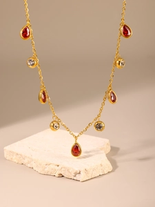 Detail view of a gold-plated teardrop necklace with red and clear crystals on a stone