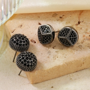 Detail view of two pairs of black cubic zirconia pavé round stud earrings on stone base