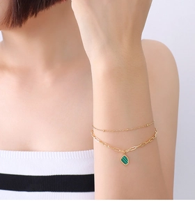 Detail of a double-layer gold chain bracelet with a green malachite gemstone pendant