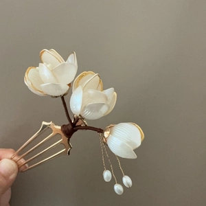 Détail d'une épingle à cheveux magnolia blanc avec bordure dorée et glands en perles