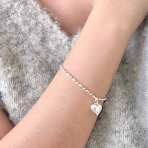 Close-up of 925 sterling silver heart charm bracelet on model wearing a knit sweater