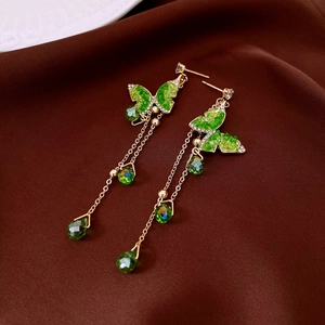 Macro shot of gold tassel butterfly earrings with emerald green crystals on silk fabric