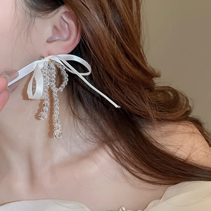 Detail showing white silk bow earrings with crystal bead tassels on a model