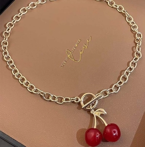 Detail shot of a golden curb chain necklace with two glossy red cherry pendants on leather