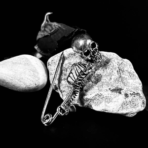 Gothic silver skull and rib cage skeleton pin brooch on dark background with dry roses