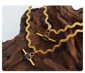 Macro detail of gold OT buckle necklace with green and black gemstones on wood