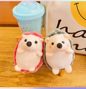 Close-up of cute plush hedgehog keychains in pink and grey on a mini wooden bench