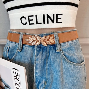 Close-up of women's brown elastic belt with golden leaf buckle on waist