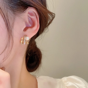 Close-up of golden geometric earrings with crystals and pearl on a model's ear