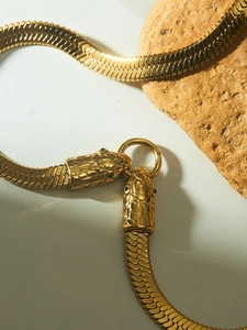 Detail of gold snake head necklace with green gemstone eyes on flat snake bone chain