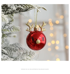 Red Christmas ball with golden antlers hanging on a snowy tree branch