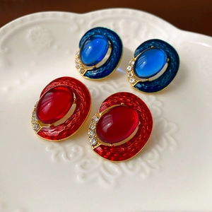 Detailed close-up of vintage oval enamel earrings with blue and red crystals in a ceramic dish