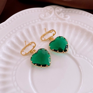 Detail of vintage gold heart earrings with emerald green crystals on a white ceramic plate