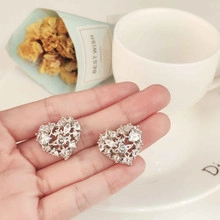 Macro detail of silver hollow heart-shaped stud earrings with clear zircon stones