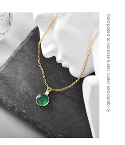 Close-up of gold plated necklace with green round gemstone on white gypsum statue
