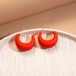 Close-up of matte red crescent-shaped acrylic earrings with silver needle post