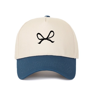 Detail of two-tone beige and navy truck hat featuring black bow embroidery on the crown