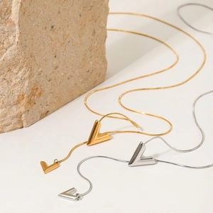 Minimalist V-shaped gold and silver necklaces on stone background with sleek snake chain