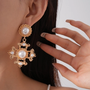 Detail shot of vintage golden cross earrings with baroque pearls worn on model ear