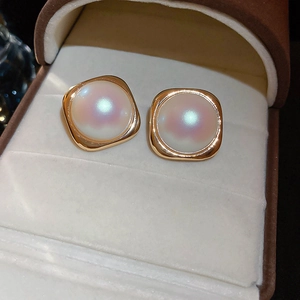 Macro shot of large white pearl earrings with square gold metal frames on velvet